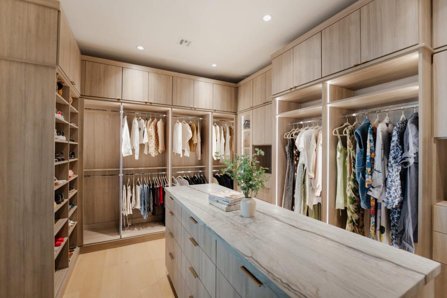 Light oak dressing room with a central island, lit hanging rails on both walls and full-height shoe shelving