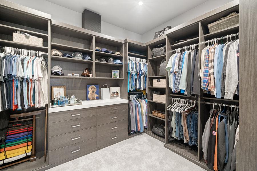 Grey woodgrain walk-in closet with double hanging rails, open shelving and a drawer bank under a white counter