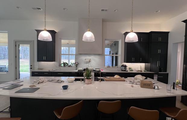 Wide view of a charcoal kitchen with a large quartz island and three pendants