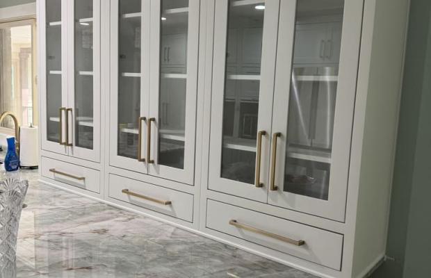 Cream glass-front wall cabinets with brass pulls above a stone counter