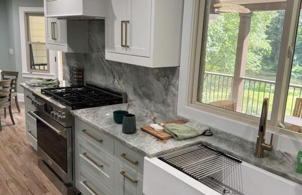 Grey-green base run with a farmhouse apron sink and a stone backsplash