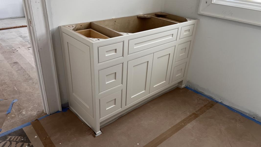 A white base cabinet standing in a room under construction, floor papered, before countertops