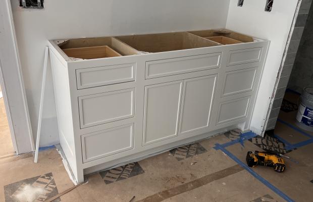 White double vanity base with open plywood drawer boxes, bathroom under construction