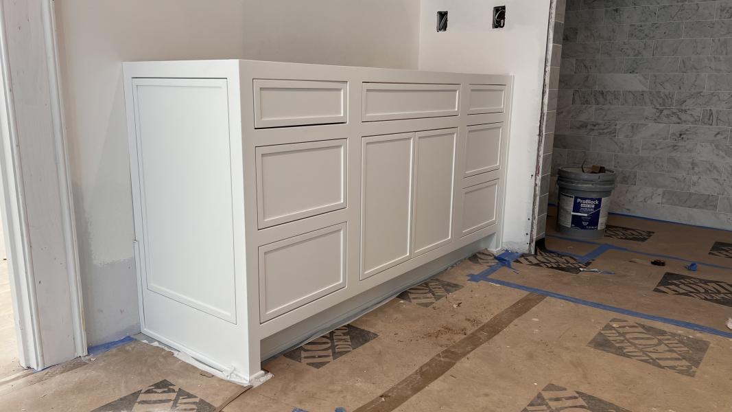 A cream raised-panel base cabinet set against a marble-tiled wall on a Rest Cabinetry install