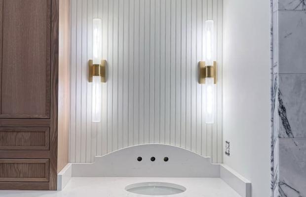 Walnut vanity beneath white beadboard with paired brass sconces