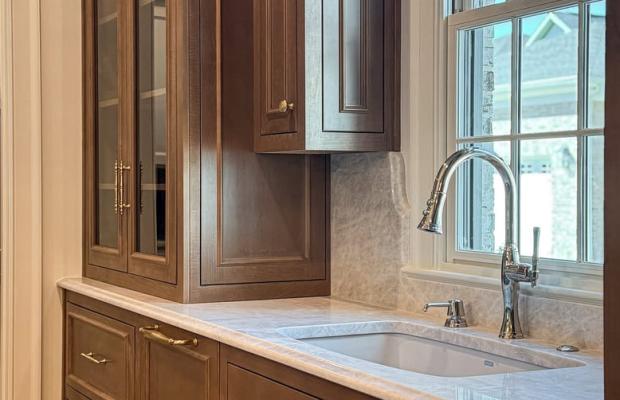 Walnut kitchen run with a sink under the window and a glass-front upper cabinet