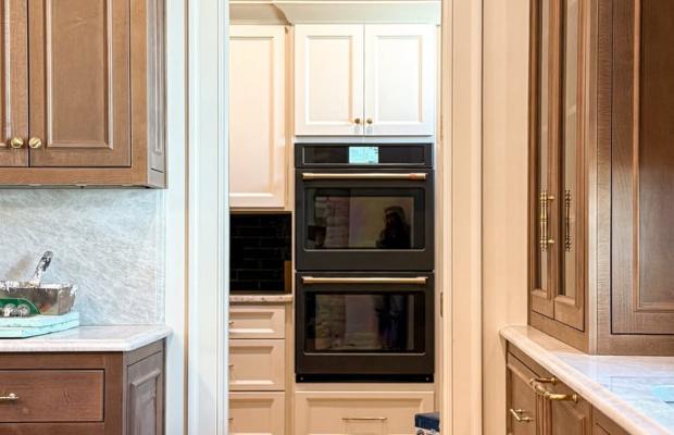 Walnut cabinetry framing the doorway through to a cream kitchen with wall ovens