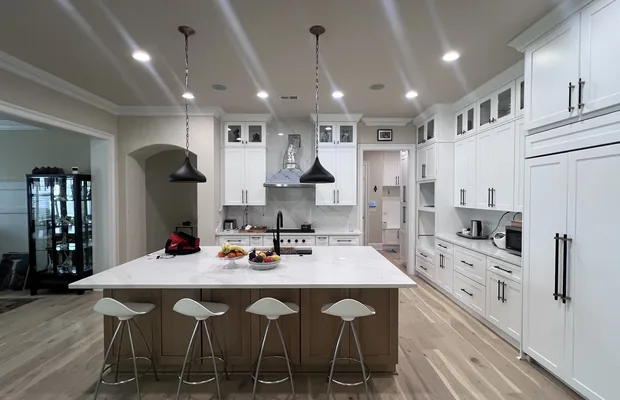 White kitchen with a long island on a natural wood base under two black pendants