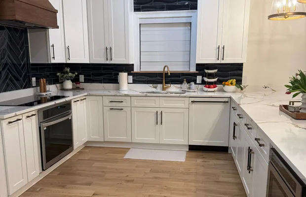 White shaker kitchen with a wood range hood, black tile backsplash and brass faucet
