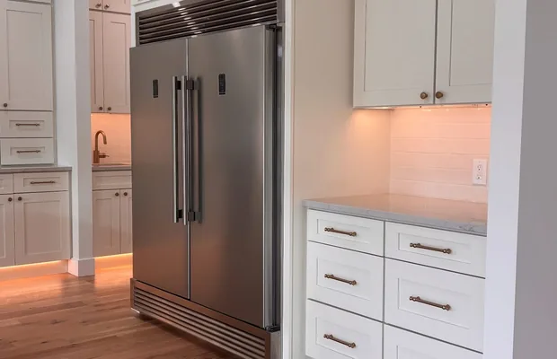 White shaker cabinets around a built-in stainless refrigerator with toe-kick lighting